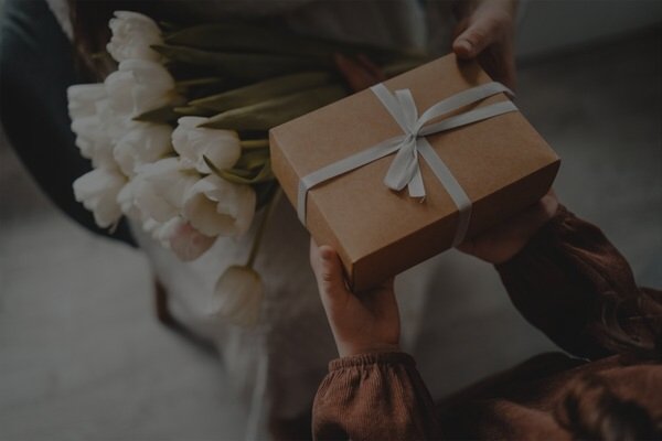 une personne offre un cadeau et des fleurs &agrave; une personne